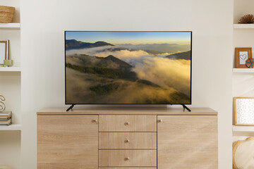 Modern TV set on wooden stand in room. Scene of nature themed movie on screen