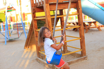The girl rides on a swing in the playground. Children's outdoor carousels