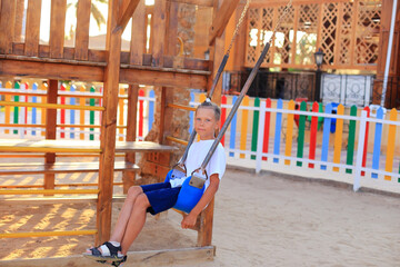 The girl rides on a swing in the playground. Children's outdoor carousels