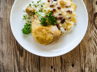 Boiled chicken thigh with white rice and lemon creamy sauce with raisins on wooden table