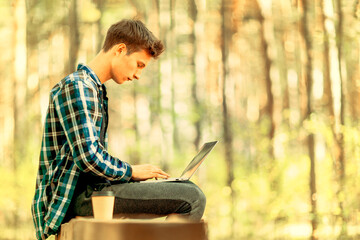 A boy is doing his homework on the laptop on a peace of nature.
