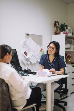 Smiling female doctor showing in vitro fertilization chart while discussing with patient in office at hospital