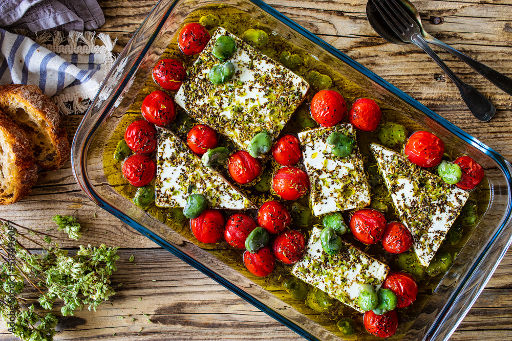 Sticker roasted tomatoes with feta cheese and broad bean served in glass pan on wooden table