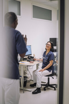 Smiling female doctor talking with male colleague standing at doorway in medical clinic
