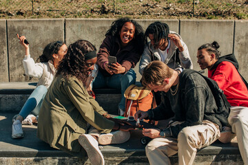 Happy man applying nail polish on hand of woman while sitting by cheerful friends in park