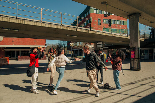 Multiracial friends applauding at young man and woman dancing at street on sunny day
