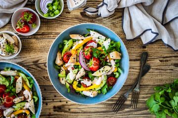 Tasty salad - fried chicken breast, strawberries, mini tomatoes and fresh green vegetables on wooden background
