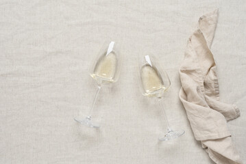 Flat lay two glasses of white wine on a beige linen tablecloth. View from above.