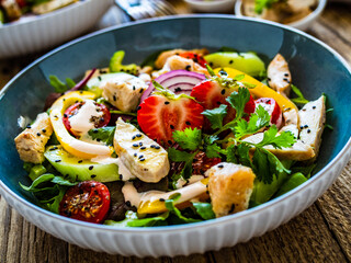 Tasty salad - fried chicken breast, strawberries, mini tomatoes and fresh green vegetables on wooden background
