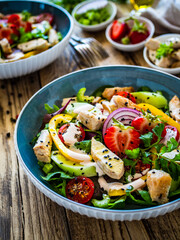 Tasty salad - fried chicken breast, strawberries, mini tomatoes and fresh green vegetables on wooden background
