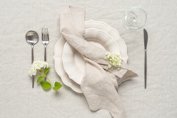 Wedding table setting. Beige plates, a beige linen napkin and white hydrangea flowers on a beige...