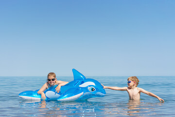 Kids are playing the sea. Little baby boys and girl in goggles with inflatable toy float shark and dolphin playing in the water on summer vacation. Babyproof on the beach and sea