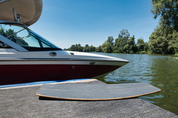 Wakeskate board lying next to a ski boat, wakeboard boat which is docked at the pier. A calm and...