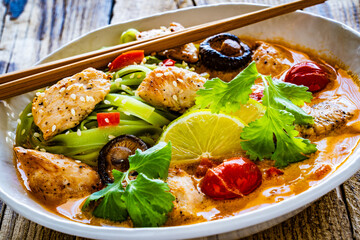 Tom Yum - Thai soup with chicken breast nuggets and rice noodles on wooden table
