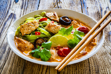 Tom Yum - Thai soup with chicken breast nuggets and rice noodles on wooden table
