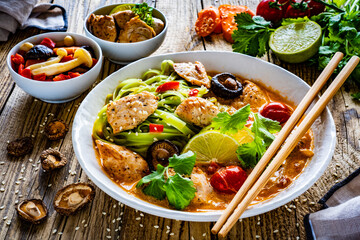 Tom Yum - Thai soup with chicken breast nuggets and rice noodles on wooden table
