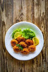 Fried breaded calamari rings with lemon and lettuce on wooden table
