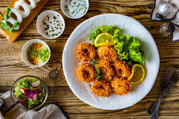 Fried breaded calamari rings with lemon and lettuce on wooden table
