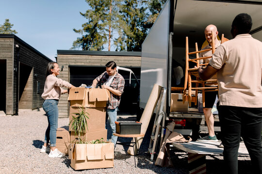Professional movers carrying chairs from truck while couple looking through boxes