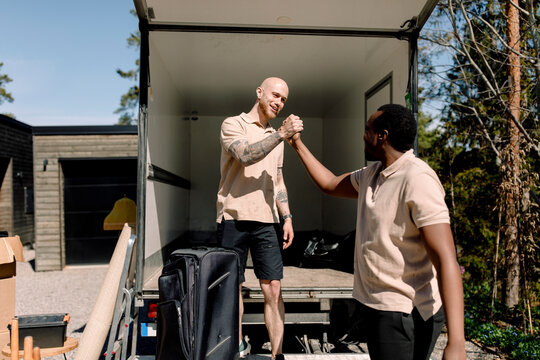 Multiracial delivery company employees shaking hands while standing outside truck