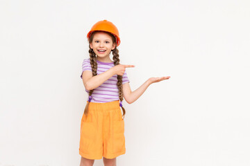 A little girl in a construction helmet holds your advertisement on her hand on a white isolated background. The concept of renovation in the children's room.