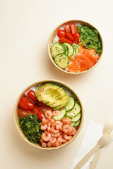 Trendy wholesome dish poke or buddha bowl - rice, wakame seaweed, tomatoes, cucumber, and red fish salmon - in a recycled round carton with sustainable fork, takeaway food concept on beige background
