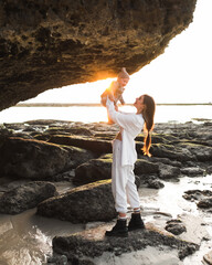 Stylish Mom holds a baby in her arms, against the backdrop of a sunset on the beach.