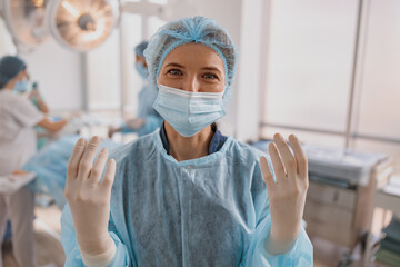 Portrait of female surgeon in mask and gloves standing in operating room, ready to work on patient
