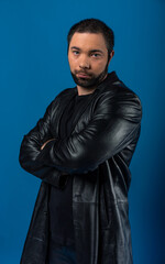 portrait of a man in a studio in a black leather coat. model with a beard on a blue background.