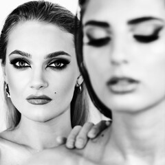 Beauty, fashion and makeup concept. Two Sexy looking woman with fancy evening makeup studio portrait. Blonde model is in camera focus and touching other model neck with hand. Black and white image