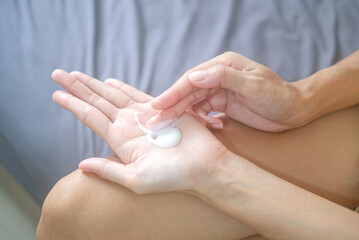 Asia woman sitting on bed and applying cream on her hand.