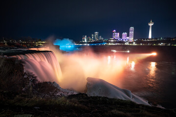 Naklejka na ściany i meble Night illumination on American Falls at Niagara Falls are pouring water through frozen landscape at winter