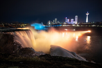Naklejka na ściany i meble Night illumination on American Falls at Niagara Falls are pouring water through frozen landscape at winter