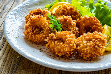 Fried breaded calamari rings with lemon and lettuce on wooden table
