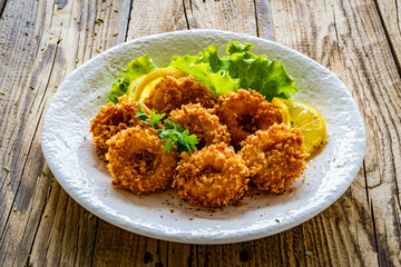 Fried breaded calamari rings with lemon and lettuce on wooden table
