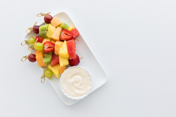 A pile of fresh fruit skewers served with yogurt dip. Copy space to the right.