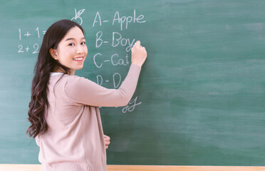 Portrait of smiling Asian teacher woman writing on chalkboard, teach english and math to students...