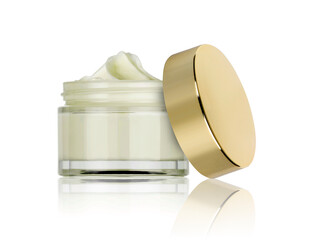 glass jar of beauty cream with golden lid resting on the side and reflected in the white plane