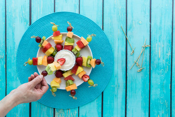 Top down view of a platter of fresh fruit kebabs with yogurt dip in the middle.
