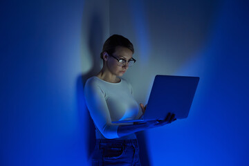 Confident young woman working on laptop against a wall with blue lighting