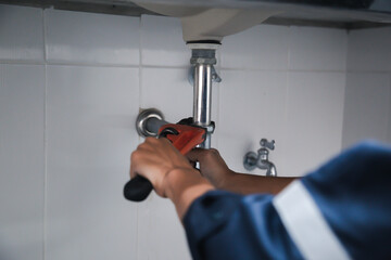 Male Plumber Using Wrench To Fix Leaking Sink In Home Bathroom.
