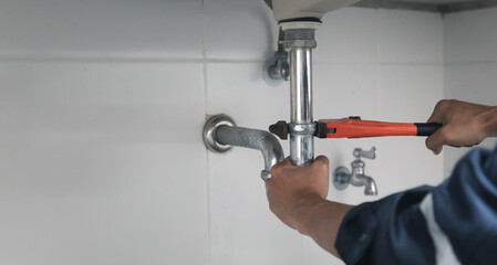 Male Plumber Using Wrench To Fix Leaking Sink In Home Bathroom.