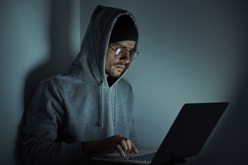 Confident young man in hooded shirt using computer while working late