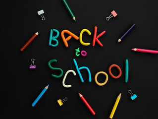 words of multi-colored plasticine back to school and school supplies felt-tip pens, pen, paper clips, on black background top view