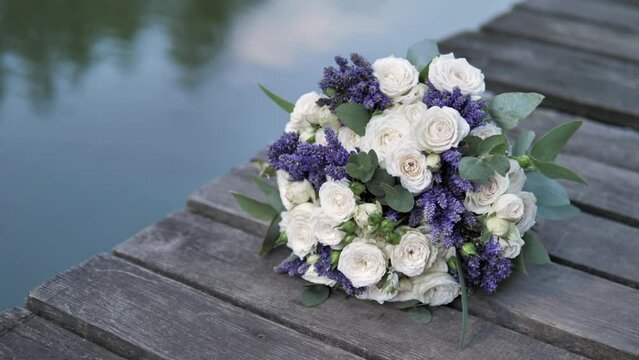 A beautiful white and purple wedding bouquet lying on the pier by the water.