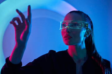Confident young woman in futuristic glasses gesturing against colorful background