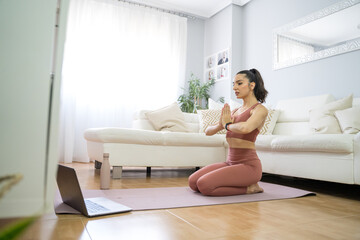 YOUNG GIRL DOING YOGA AND PILATES IN THE LIVING ROOM OF HER HOME WITH THE COMPUTER
