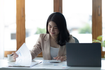 Asian Businesswoman using a calculator and laptop computer for doing math finance on a wooden desk, tax, accounting, statistics report and analytical research concept.