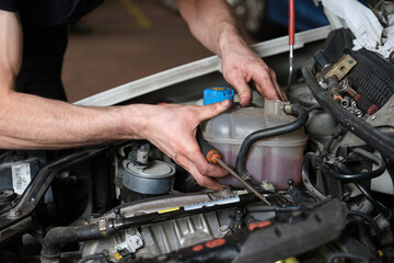Fototapeta na wymiar Car mechanic hands replacing antifreeze container. Mechanics workshop.