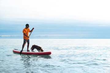 a guy on a sup board with a paddle with a dog stands on the sea in summer